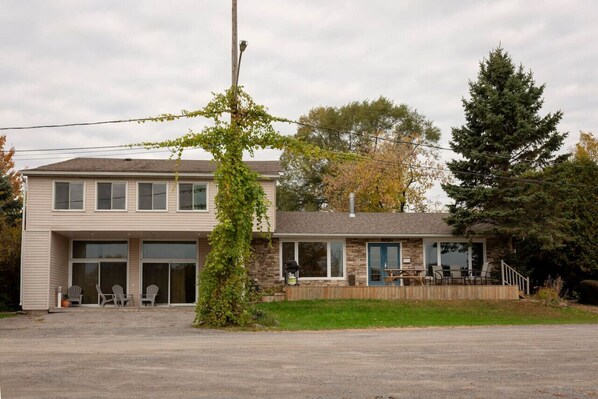 A two-story building with a covered patio area, a stone facade, and a large tree in front.
