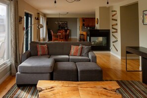 A modern living room with a sectional sofa, a wooden coffee table, and a dining area in the background.
