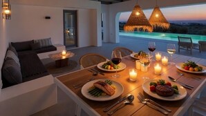 A dining area with a table set for two, candles, and a view of the ocean at dusk. - Faragas Hill (Paros Island)