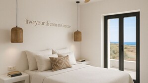 A modern bedroom with a large bed, two bedside tables, a ceiling fan, and a view of the sea through a large window. - Faragas Hill (Paros Island)
