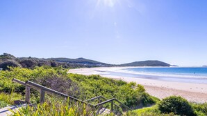 A beach with a wooden staircase leading down to the shore, surrounded by greenery.