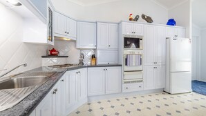A modern kitchen with white cabinetry, a granite countertop, a stainless steel sink, a double oven, and a refrigerator.