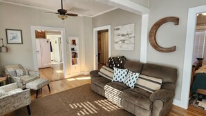 A living room with a brown sofa, a patterned armchair, and a coffee table. There is a ceiling fan, a framed picture on the wall, and a large letter 'C' decoration. - Lakeview, 4 beds, boat parking & ramp, at Red Arrow Marina (Afton)