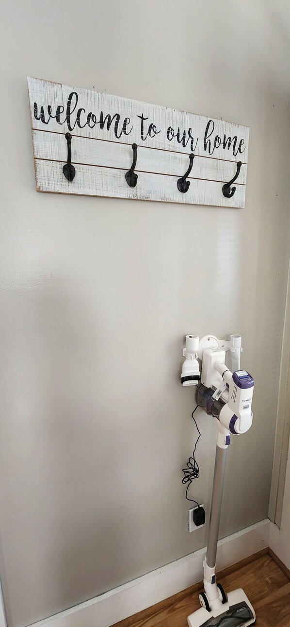 Un panneau fixé au mur, muni de crochets, et un aspirateur appuyés contre un mur uni.