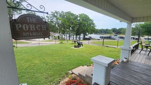 A porch with a sign reading "The Porch Sit & Relax" overlooking a grassy area with a view of a lake and boats. - Lakeview, 4 beds, boat parking & ramp, at Red Arrow Marina (Afton)