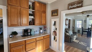 A kitchen with wooden cabinets, a coffee maker, and a countertop with various items. There is a dining area with a couch and a rug. - Lakeview, 4 beds, boat parking & ramp, at Red Arrow Marina (Afton)