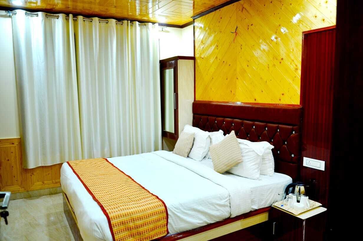 A hotel room with a large bed, a wooden headboard, a bedside table with a lamp, and a window with curtains.