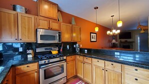 A kitchen with wooden cabinets, stainless steel appliances, and a black countertop. - Chalet 98 at the Official Collins Lake Resort (Government Camp)