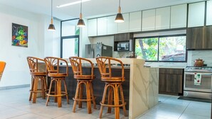 Een moderne keuken met een centraal eiland, barkrukken, roestvrijstalen apparatuur en een groot raam met uitzicht op groen.