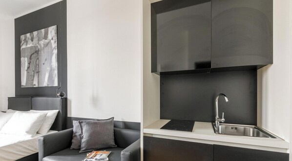 A modern bedroom with a bed, a gray sofa, and a magazine on the sofa. The image also shows a kitchen with a sink and a stove. - Chic Studio in Historical Bovisa, Milan (Milan)