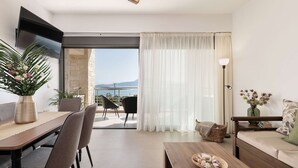 A modern living room with a dining area, a sofa, a TV mounted on the wall, and a view of the sea through large windows. - Stone villa with private heated pool close to Marathi beach (Kounoupidiana)