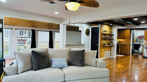 A living room with a sofa, a ceiling fan, and a kitchen area visible through an open door.