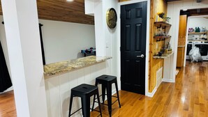 A kitchen with wooden flooring, a black door, and a bar area with stools.