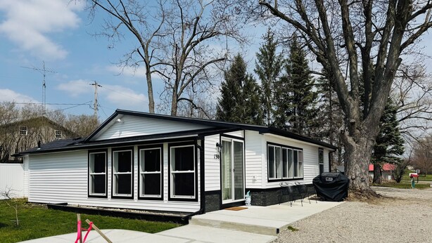 A single-story house with a black roof and white siding, a front door, and a small porch area.