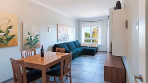 A modern living room with a sectional sofa, a dining table with chairs, and artwork on the walls. - Camelot - Apartment (Oliva)