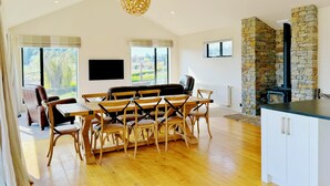 A spacious dining area with a wooden table and chairs, a stone fireplace, and a large window offering a view of the outdoors. - Cedar View (Lake Tekapo)