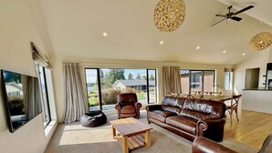 A spacious living room with a leather sofa, a wooden coffee table, and a black bean bag. There is a large window providing a view of the outdoors. - Cedar View (Lake Tekapo)