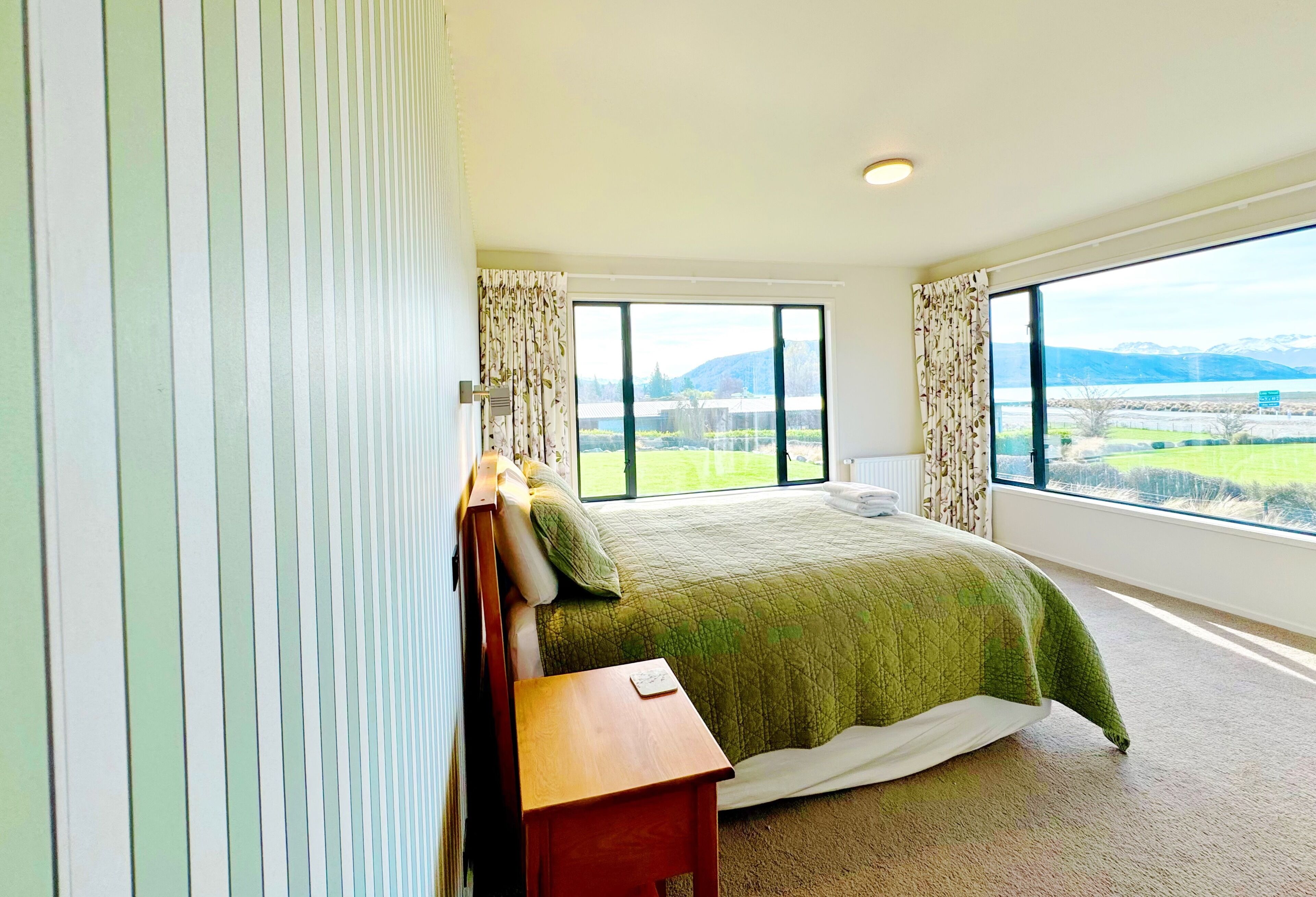 Un dormitorio con una cama grande, una mesita de noche y vistas a un lago y montañas.