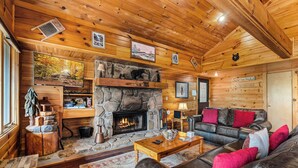 A cozy cabin interior with a stone fireplace, wooden walls, a leather sofa, and a dining area. - Dancing in the Moonlight is the Perfect Romantic Getaway (GATLINBURG)