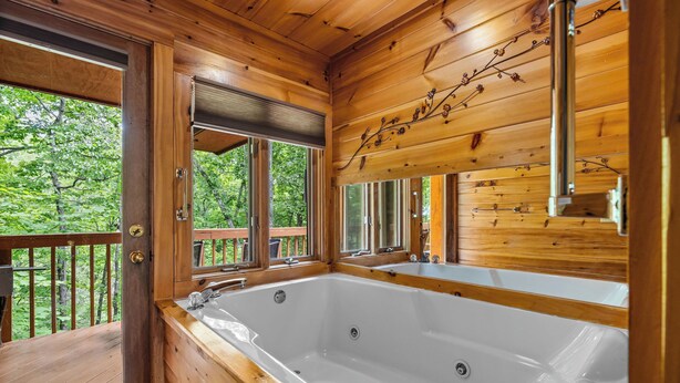 A wooden cabin with a large bathtub and a deck with a view of trees. - Dancing in the Moonlight is the Perfect Romantic Getaway (GATLINBURG)
