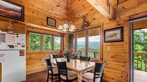A wooden cabin with a dining table and chairs, large windows, and a refrigerator. - Dancing in the Moonlight is the Perfect Romantic Getaway (GATLINBURG)