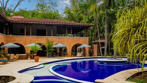 A swimming pool with a curved design, surrounded by a brick building with arched doorways and outdoor seating. - Casa Cielo Al Alma (Santa Fe de Antioquia)