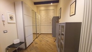 Een smalle gang met een spiegelkast, een klein bureau en een bergkast met glazen deuren.