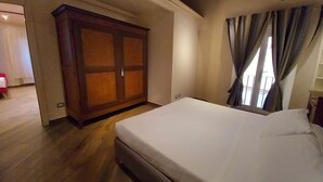 Een slaapkamer met een grote houten garderobe, een bed met witte lakens en een raam met gordijnen.