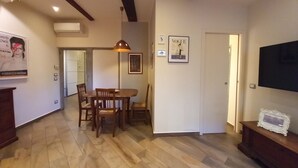 Een eetgedeelte met houten stoelen en een tafel, een plafond met zichtbare balken en een aan de muur bevestigde televisie.