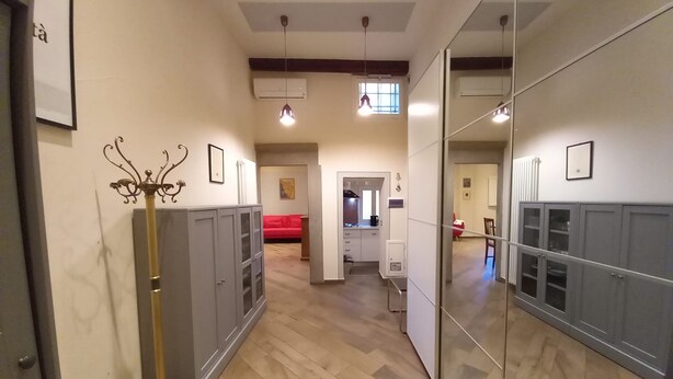 Een gang met een spiegelkast, een rode bank op de achtergrond en een keuken die zichtbaar is door een open deur.