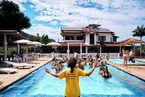 A swimming pool with people, a building with solar panels, and a clear sky. - Pousada Serra do Roncador (Saquarema)