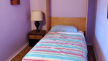 A single bed with a colorful striped bedspread in a room with purple walls and a wooden headboard.