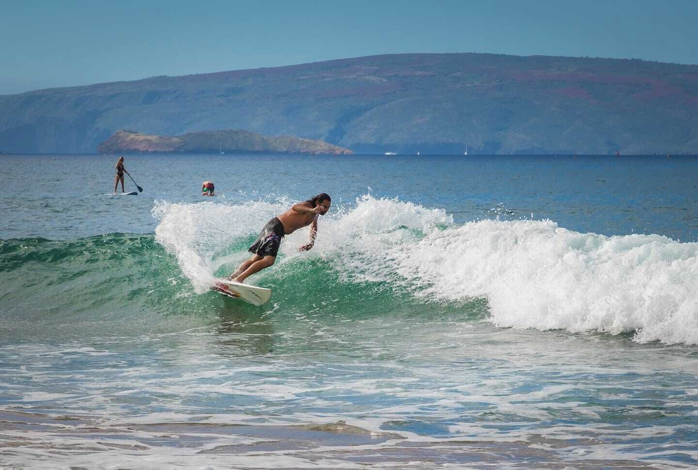 A person surfing on a wave with a mountainous landscape in the background.