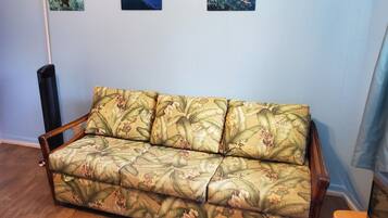 Ein Sofa mit floralem Muster, eine Wand mit drei gerahmten Bildern und ein Heizlüfter.