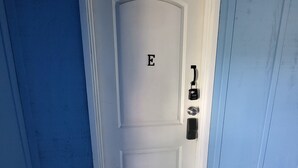 Eine weiße Tür mit einem Zahlenschloss und dem Buchstaben 'E', eingebaut in einen Raum mit blauen Wänden.