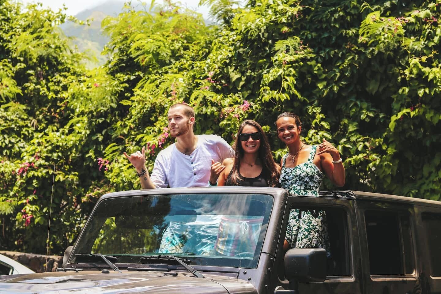 Three people standing in a vehicle with a forested background.