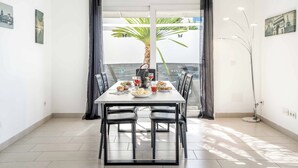 A dining area with a table set for two, a potted plant, and a view of a palm tree outside.