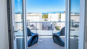 A balcony with two black chairs, a glass door, and a view of buildings and a distant landscape.