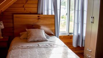 Una camera da letto con soffitto in legno, un letto con copripiumino decorato, due cuscini, un comodino con una lampada e un armadio.