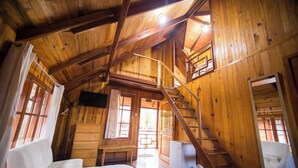 Interior de una cabaña de madera con una cama, cómoda y una escalera que sube a un altillo.