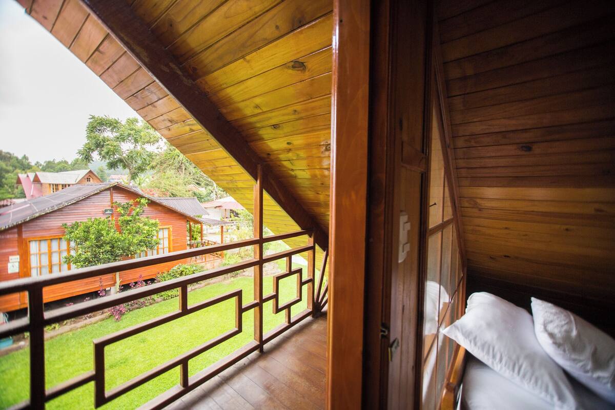 Un balcon en bois offrant une vue sur un bâtiment rouge et une pelouse verdoyante.
