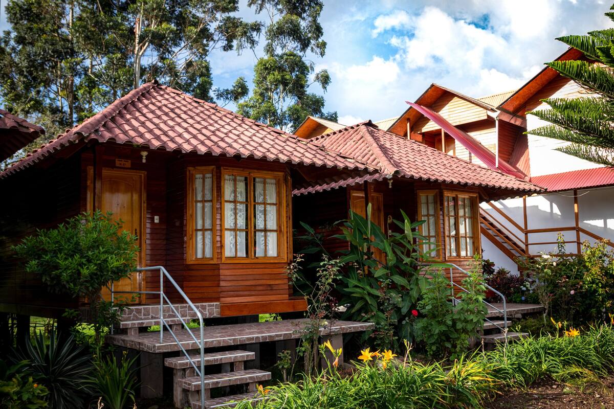 Une cabane en bois avec un toit en tuiles, entourée d’une végétation luxuriante et d’un jardin.