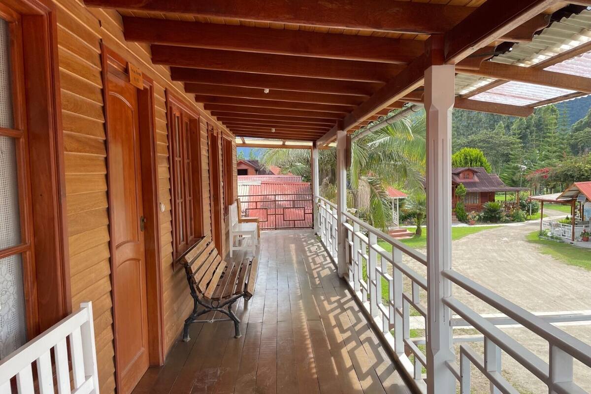Une véranda couverte avec des balustrades en bois, un banc et une vue sur un paysage rural avec des maisons et de la verdure.
