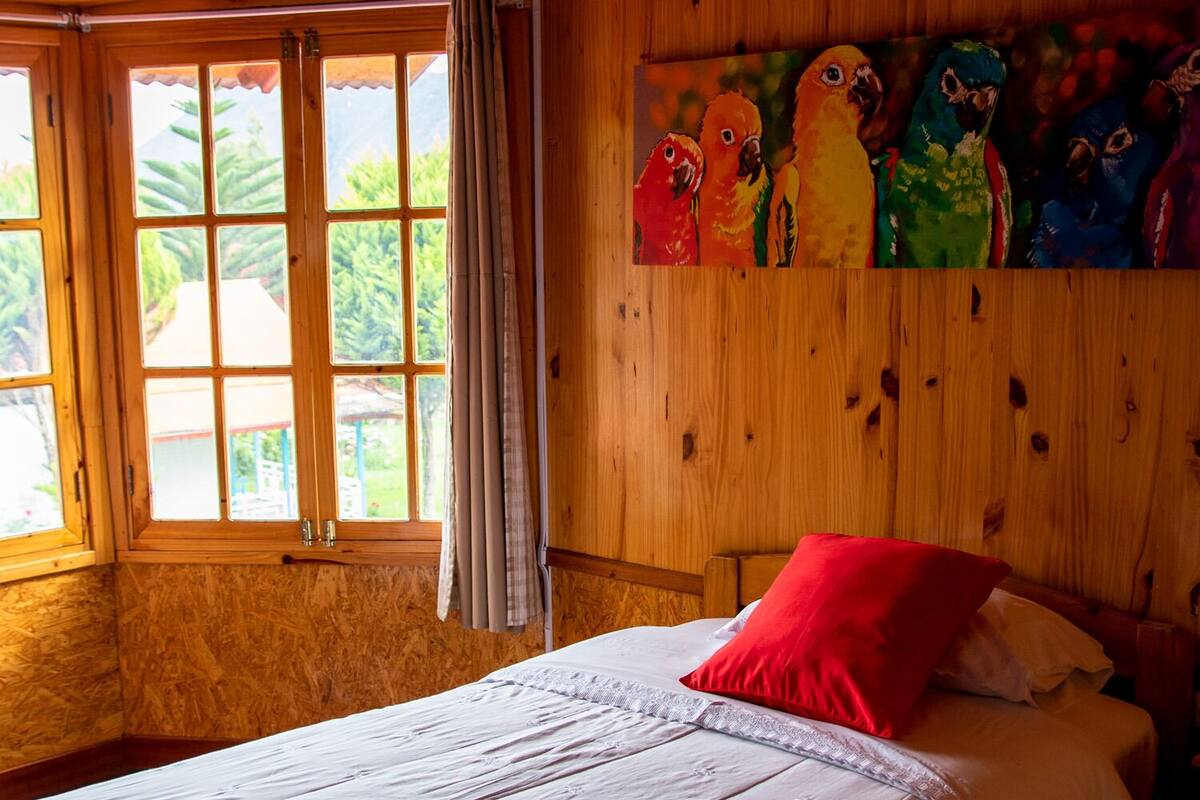 Une pièce en bois avec un lit, une fenêtre et un tableau représentant des perroquets aux couleurs vives.