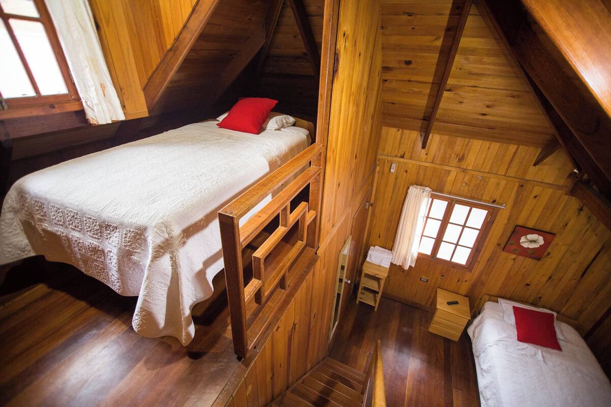 Une chambre dans un chalet en bois, avec un lit superposé, un petit bureau en bois et une fenêtre avec des rideaux.