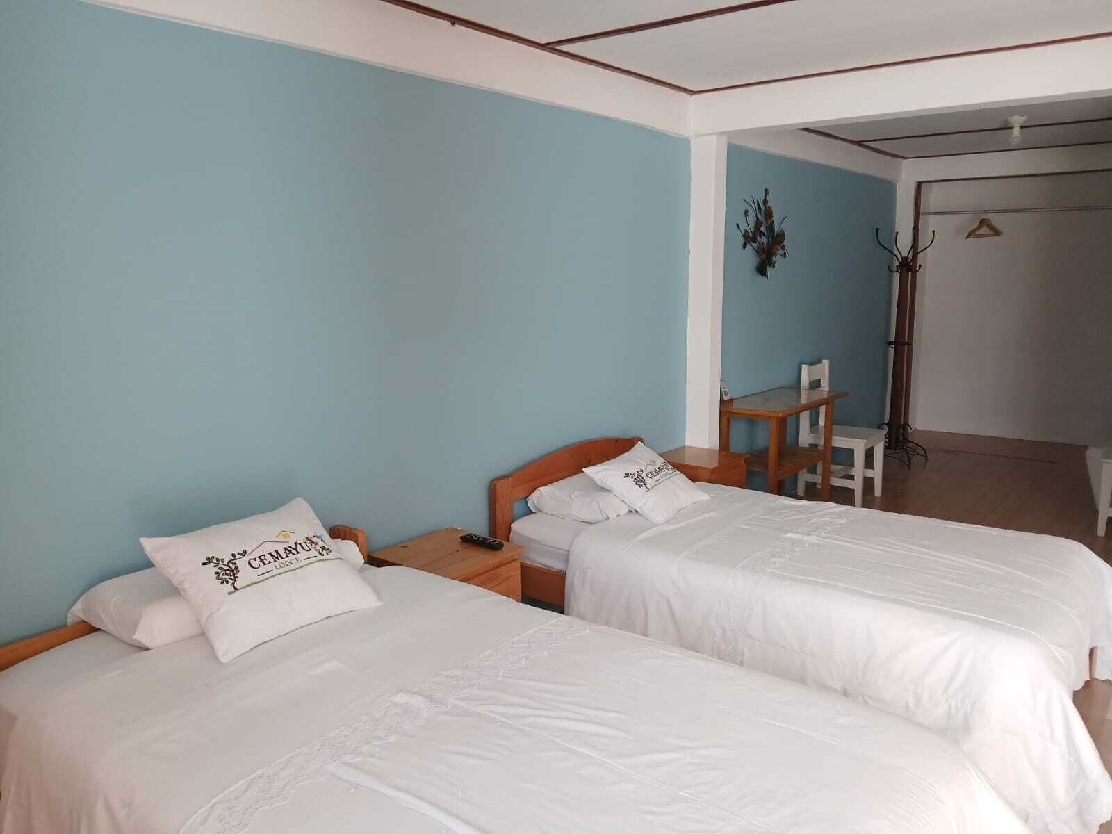 A room with two single beds, a wooden nightstand, a small table, and a chair.