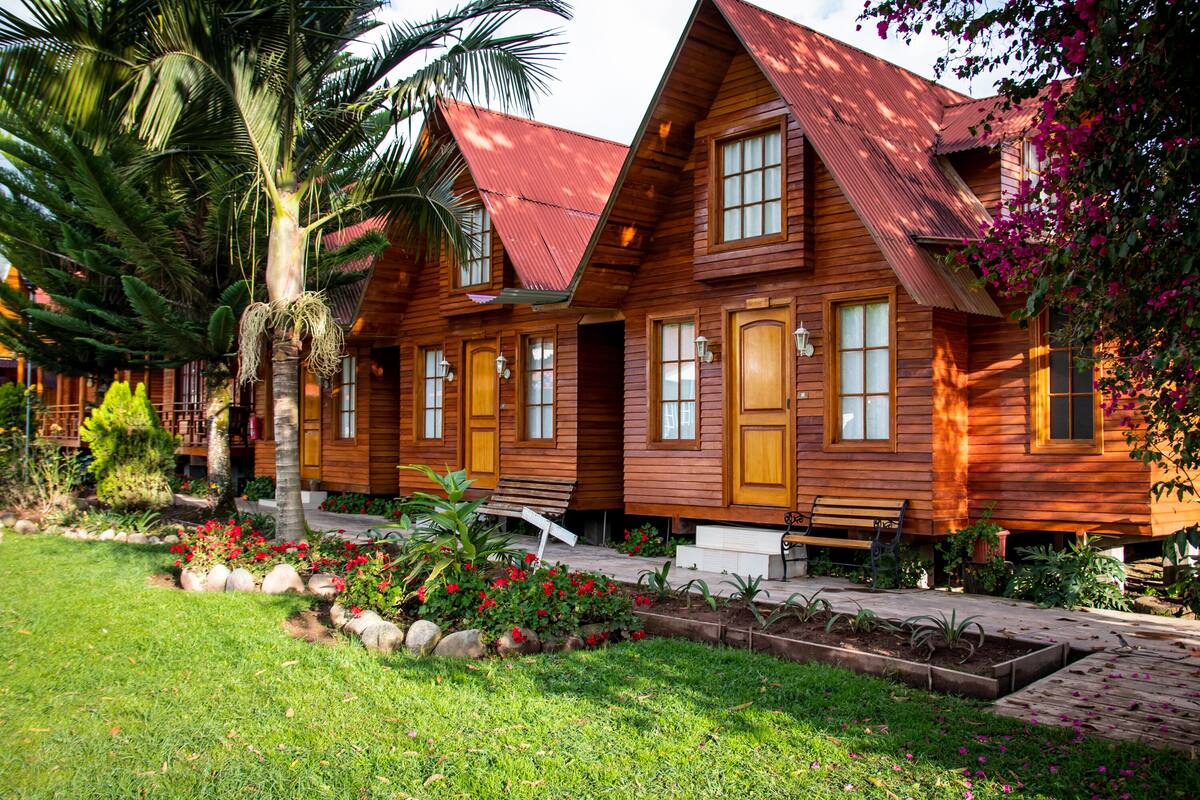 Une rangée de cabanes en bois avec un toit en pente, un palmier et un jardin parsemé de fleurs rouges.