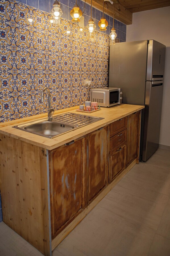 A kitchen with a wooden countertop, stainless steel sink, a microwave, and a refrigerator.