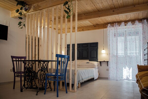 A room with a bed, a table with chairs, a TV on the wall, and a window with curtains. - Cozy studio apartment within walking distance of the Archaeological Excavations of Pompeii (Scafati)