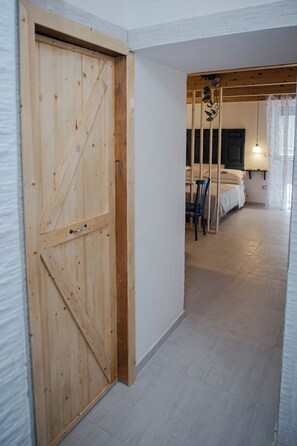 A wooden door leading into a room with a bed, a chair, and a hanging plant.